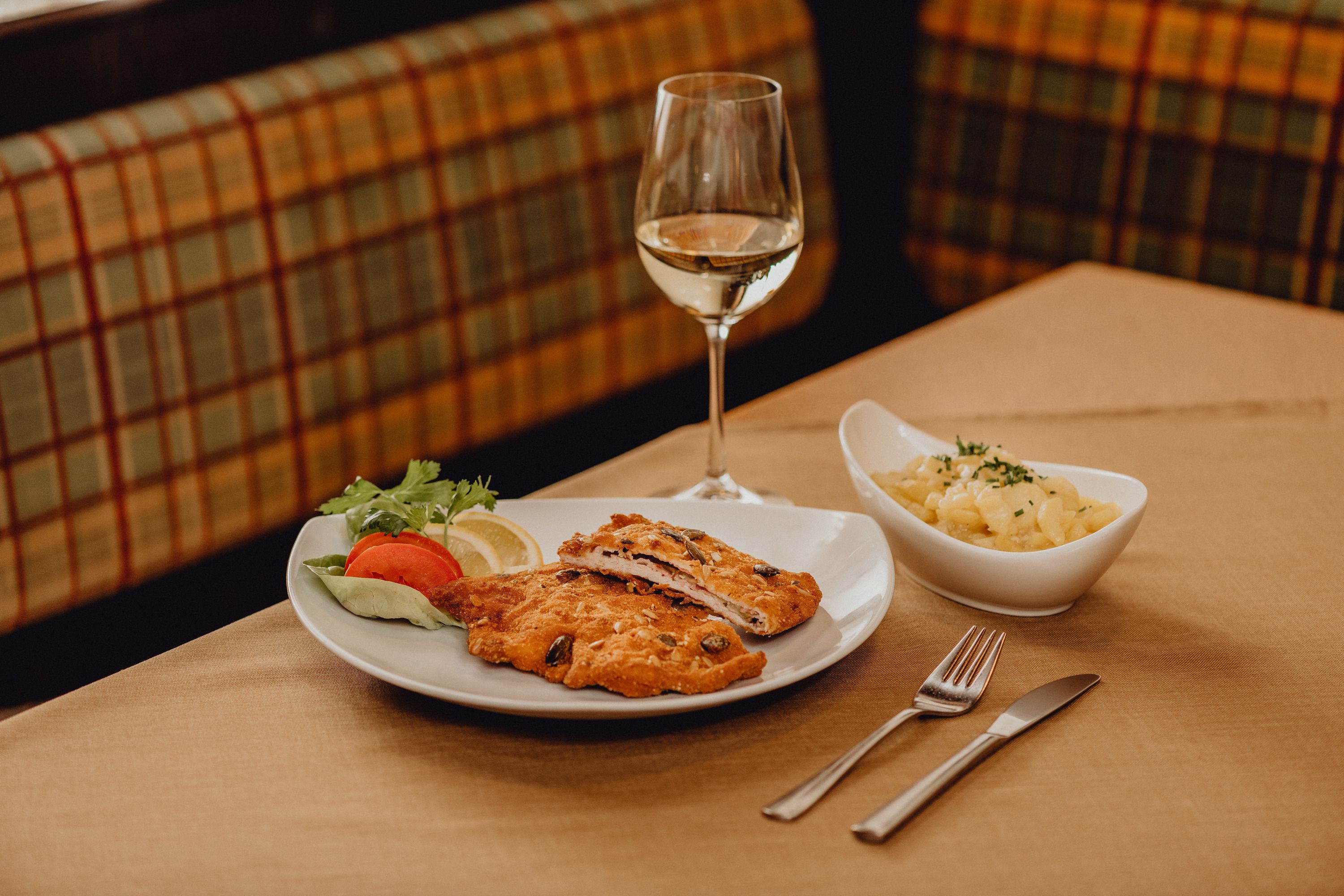 Ein Teller mit Cordon bleu, Salatgarnitur und ein Glas Weißwein auf einem Tisch.