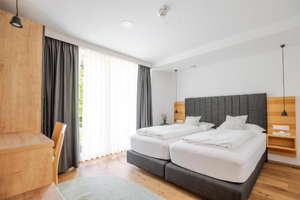 Helles Hotelzimmer im Hotel Ottenstein – Das Wohlfühlhotel mit zwei Einzelbetten, Holzdetails, Schreibtisch und großen Fenstern mit Vorhängen.