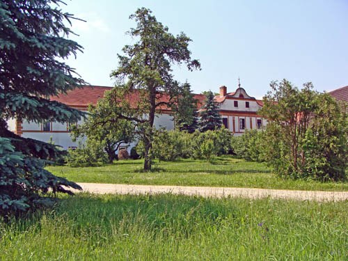 A historic building with a red roof, surrounded by trees and a green meadow.