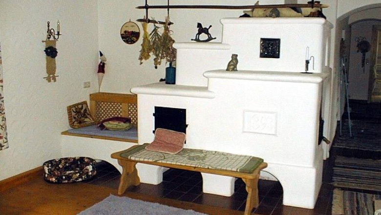 Gemütlicher Raum mit weißem Kachelofen und Holzbalken.