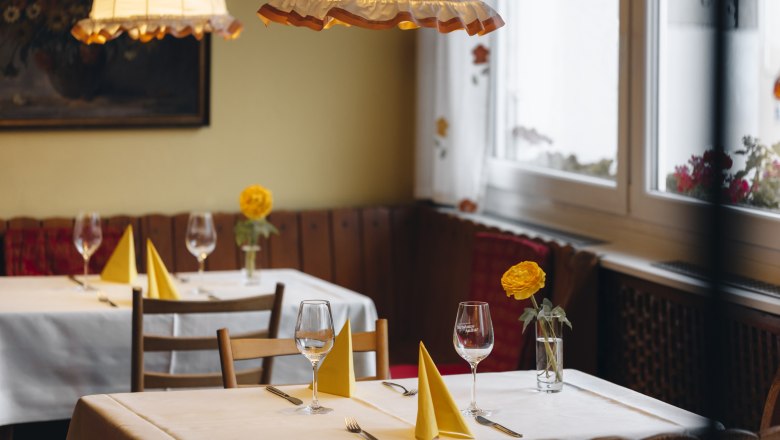 Gemütliches Restaurant mit gedeckten Tischen, gelben Servietten und Blumen.