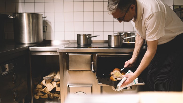 A cook takes a roasted dish out of a wood-fired oven in a restaurant kitchen.