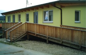 Gelbes Gebäude mit Holzrampe und Fenstern.