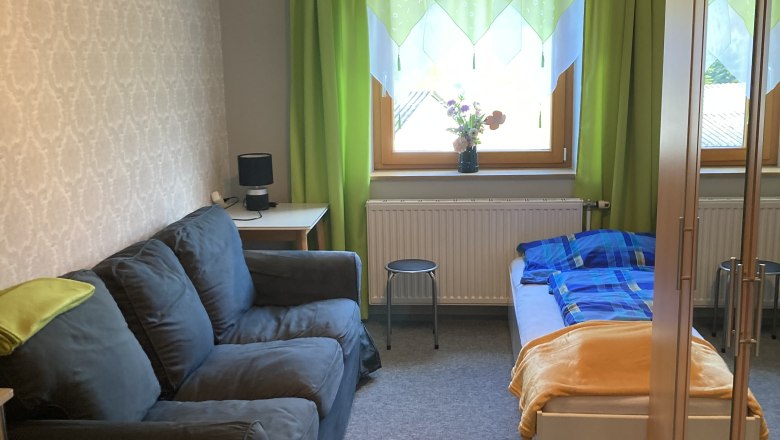 Ein gemütliches Schlafzimmer mit Sofa, Bett, Schrank und grünem Vorhang.