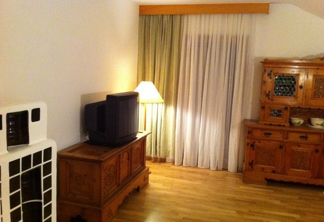 Ein Wohnzimmer mit Holzmöbeln, einem alten Fernseher, einer Stehlampe und Vorhängen.
