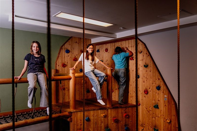 Kinder spielen in einem Indoor-Kletterbereich mit Holzwänden und bunten Klettergriffen.