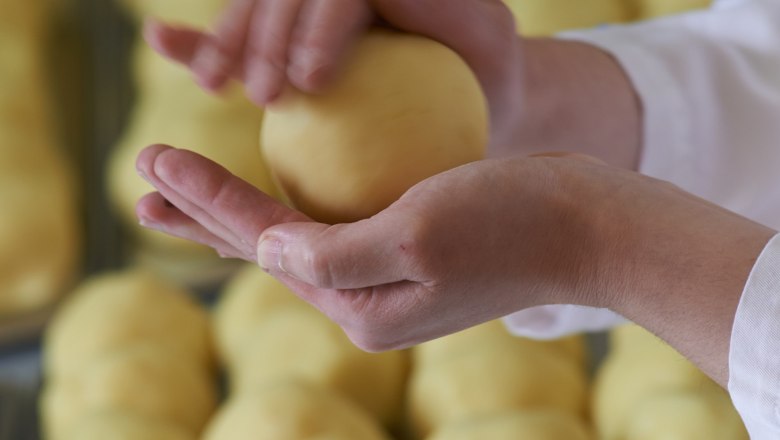 Person formt Teigkugel mit Händen, im Hintergrund weitere Teigkugeln.