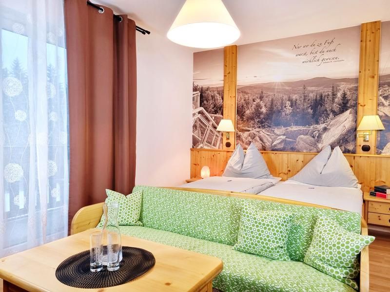 Gemütliches Doppelzimmer mit zwei Betten, grünem Sofa und großem Wandbild einer Landschaft.