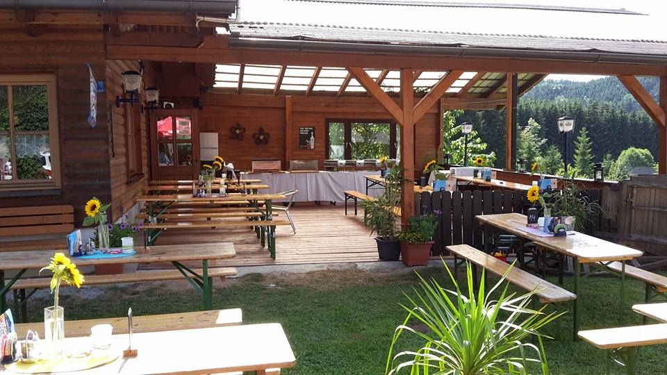 Ein gemütlicher Biergarten mit Holztischen und Bänken, dekoriert mit Sonnenblumen, umgeben von grüner Landschaft.