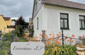 Au&szlig;enansicht eines wei&szlig;en Ferienhauses mit Garten und Blumen.