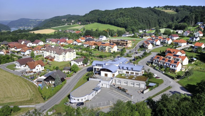 Aerial view of a village with community center and surrounding houses in a green hilly landscape.