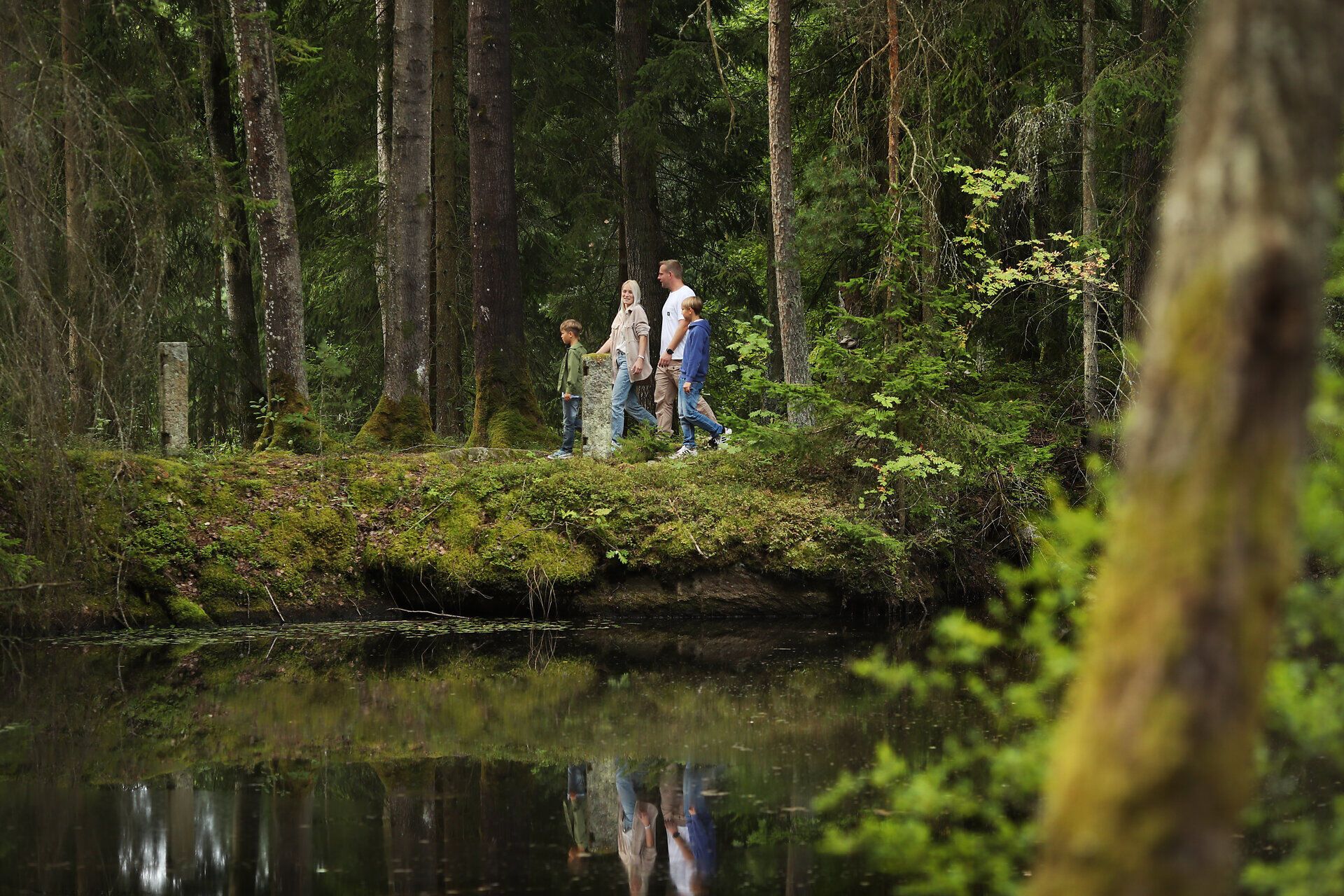 Eine Familie spaziert im Wald entlang eines Teichs. 