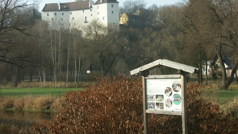 Ein Lehrpfad-Schild vor einer Burg in einer ländlichen Landschaft.