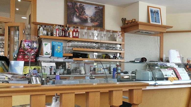 Innenansicht eines Cafés mit Theke, Gläsern und Dekorationen.