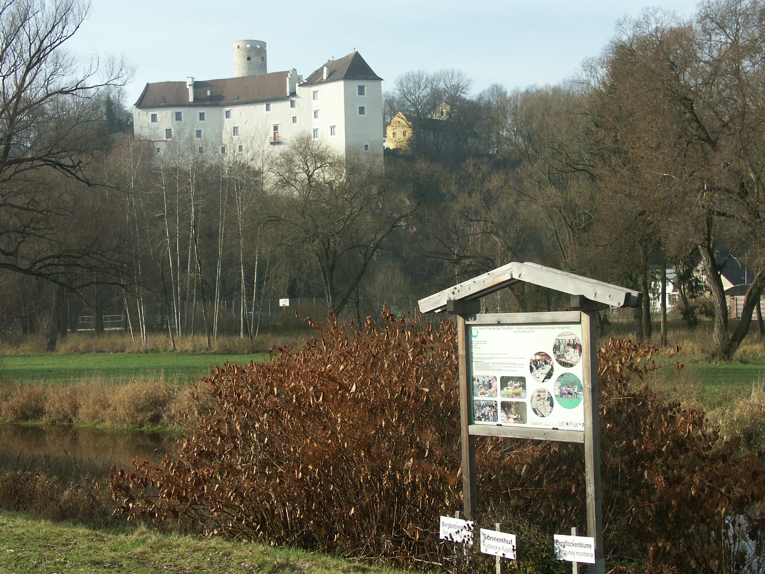 Ein Lehrpfad-Schild vor einer Burg in einer ländlichen Landschaft.