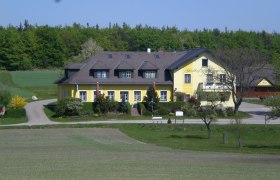 Ein gelber Gasthof in ländlicher Umgebung mit Bäumen und Wiesen.