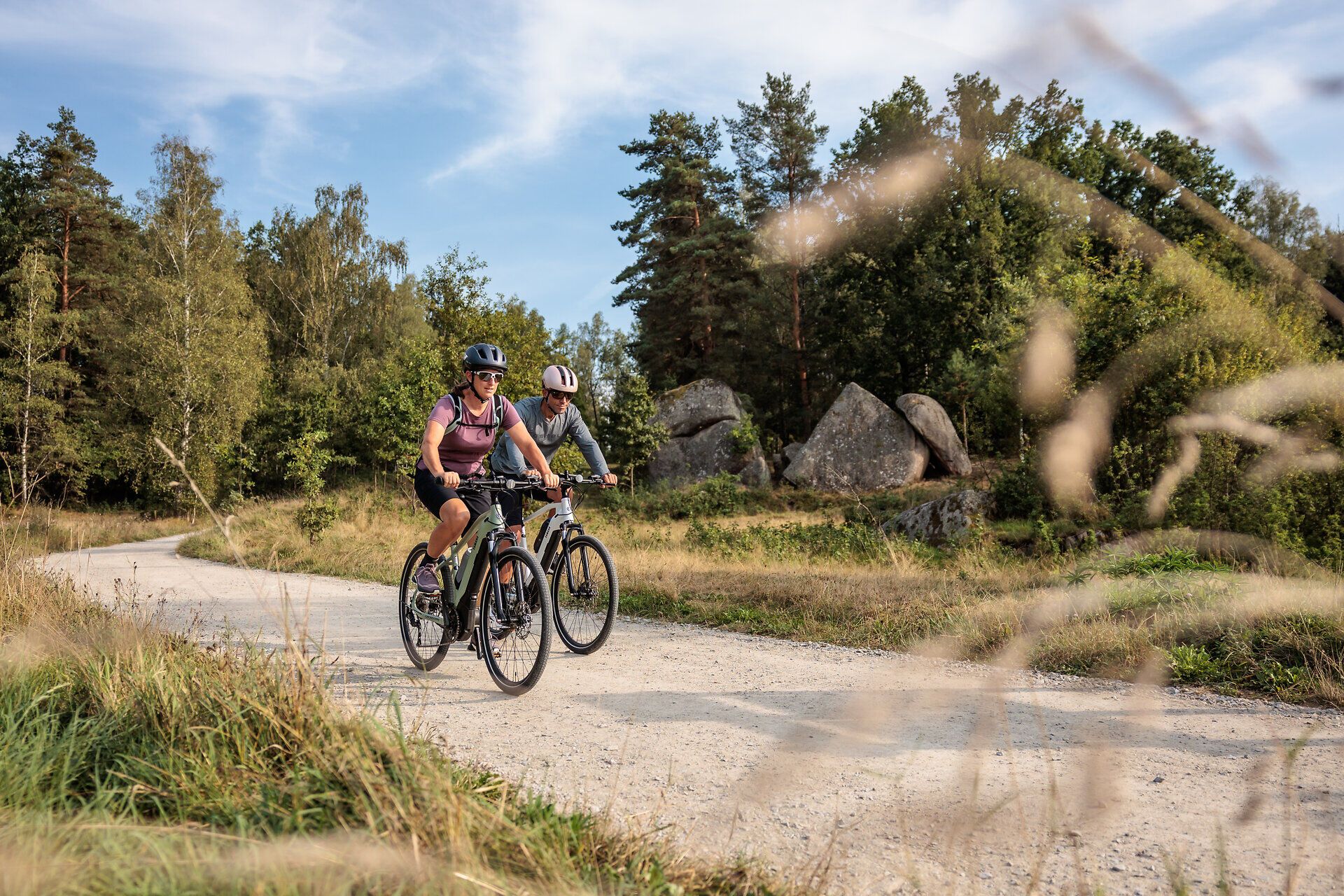 Zwei Radfahrer genießen die frische Luft und die malerische Landschaft des Naturparks. Umgeben von üppigem Grün und majestätischen Felsen, vermittelt die Szenerie ein Gefühl von Freiheit und Abenteuer. Der Weg lädt dazu ein, die Schönheit der Natur in vollen Zügen zu erleben.