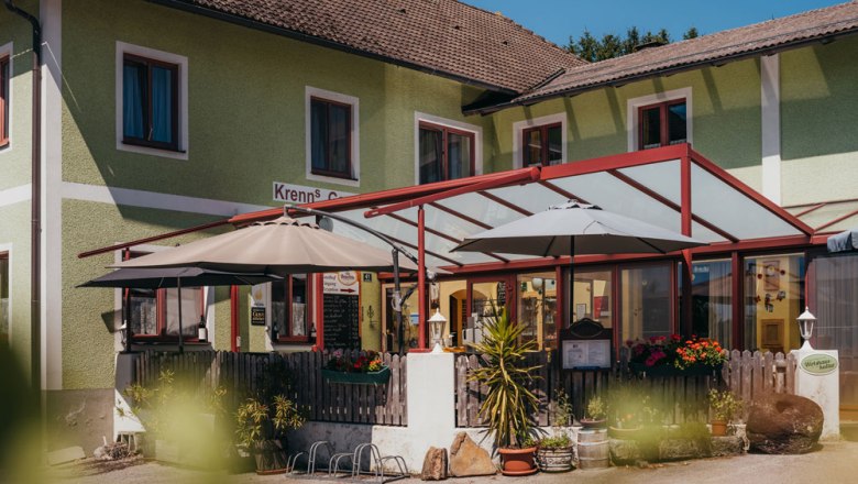 Au&szlig;enansicht eines Wirtshauses mit Terrasse und Sonnenschirmen.