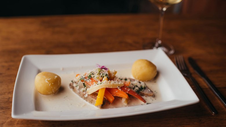 Ein Teller mit Krenfleisch, Wurzelgem&uuml;se und Kn&ouml;deln auf einem Holztisch.