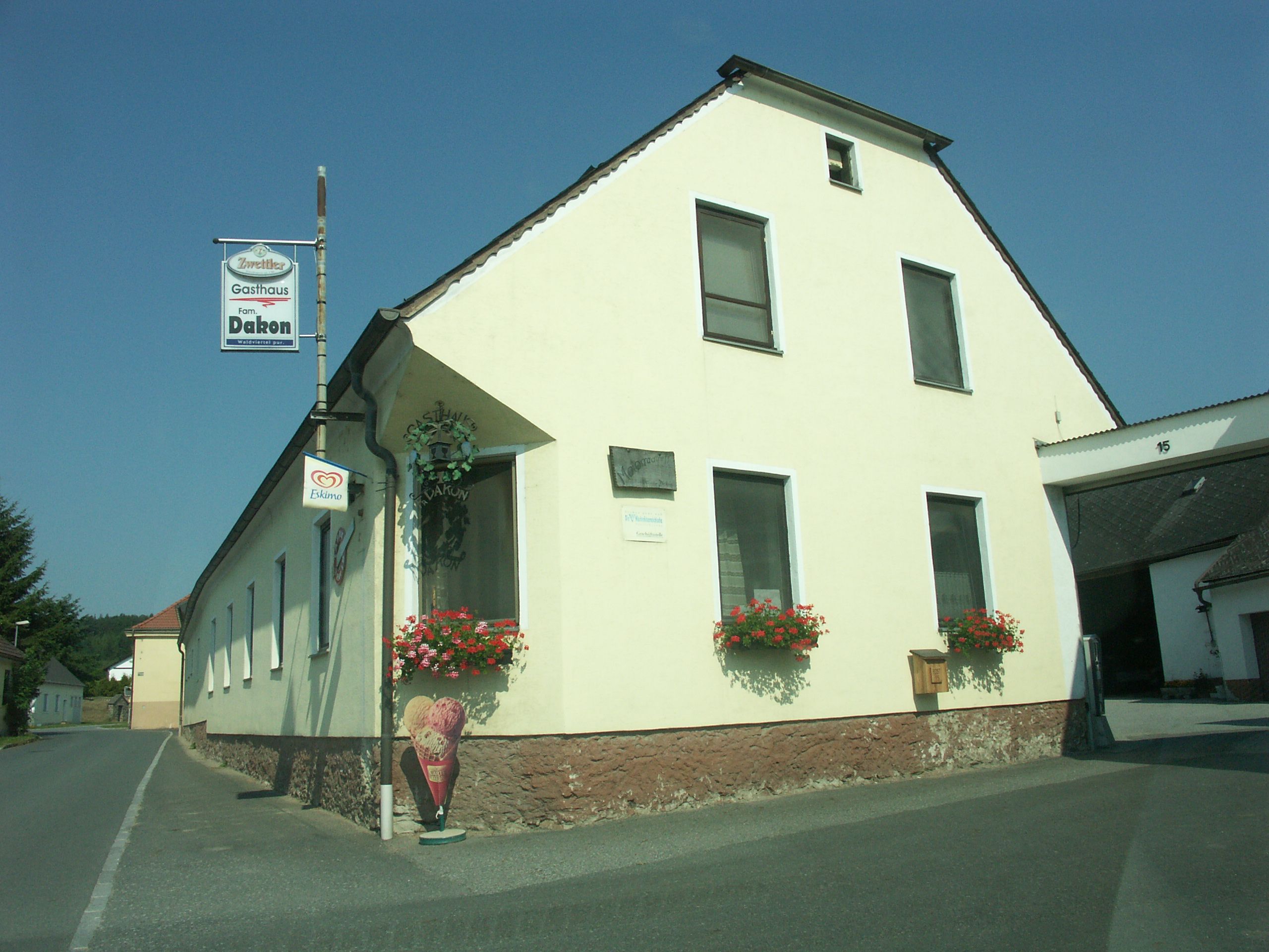 Ein gelbes Gasthaus mit Blumen und Eistafel an einer Landstraße.