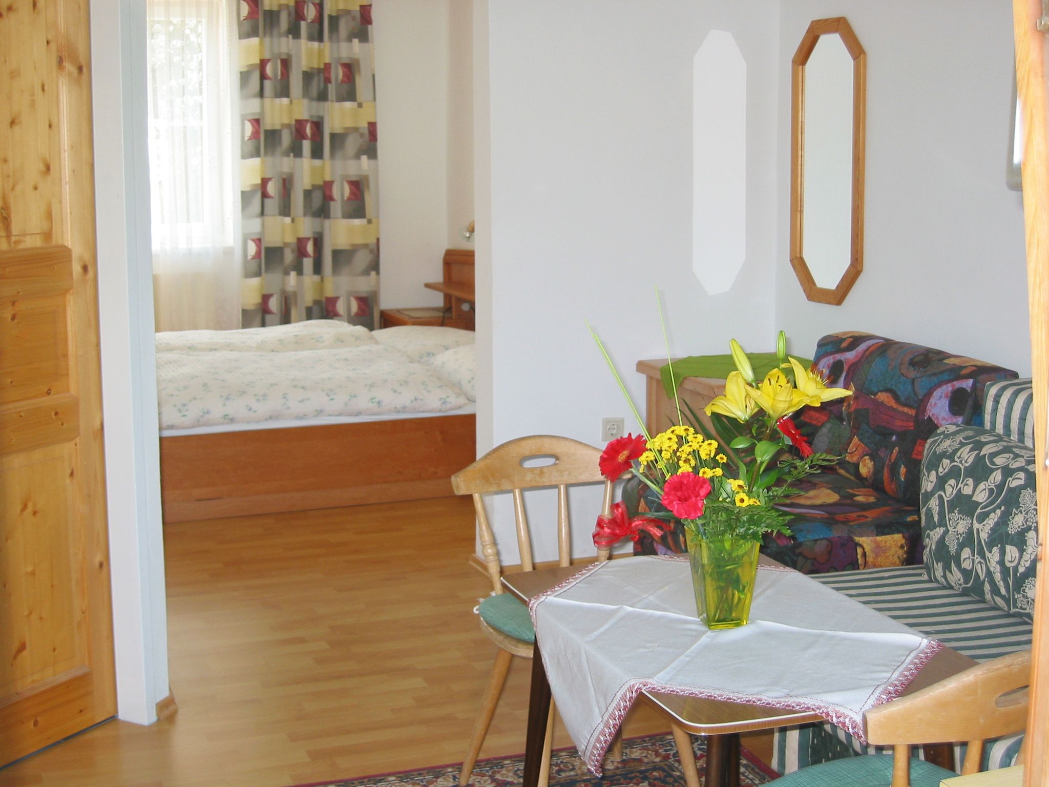 Ein gemütliches Zimmer mit Holzmöbeln, einem Bett im Hintergrund und einem Tisch mit Blumen im Vordergrund.