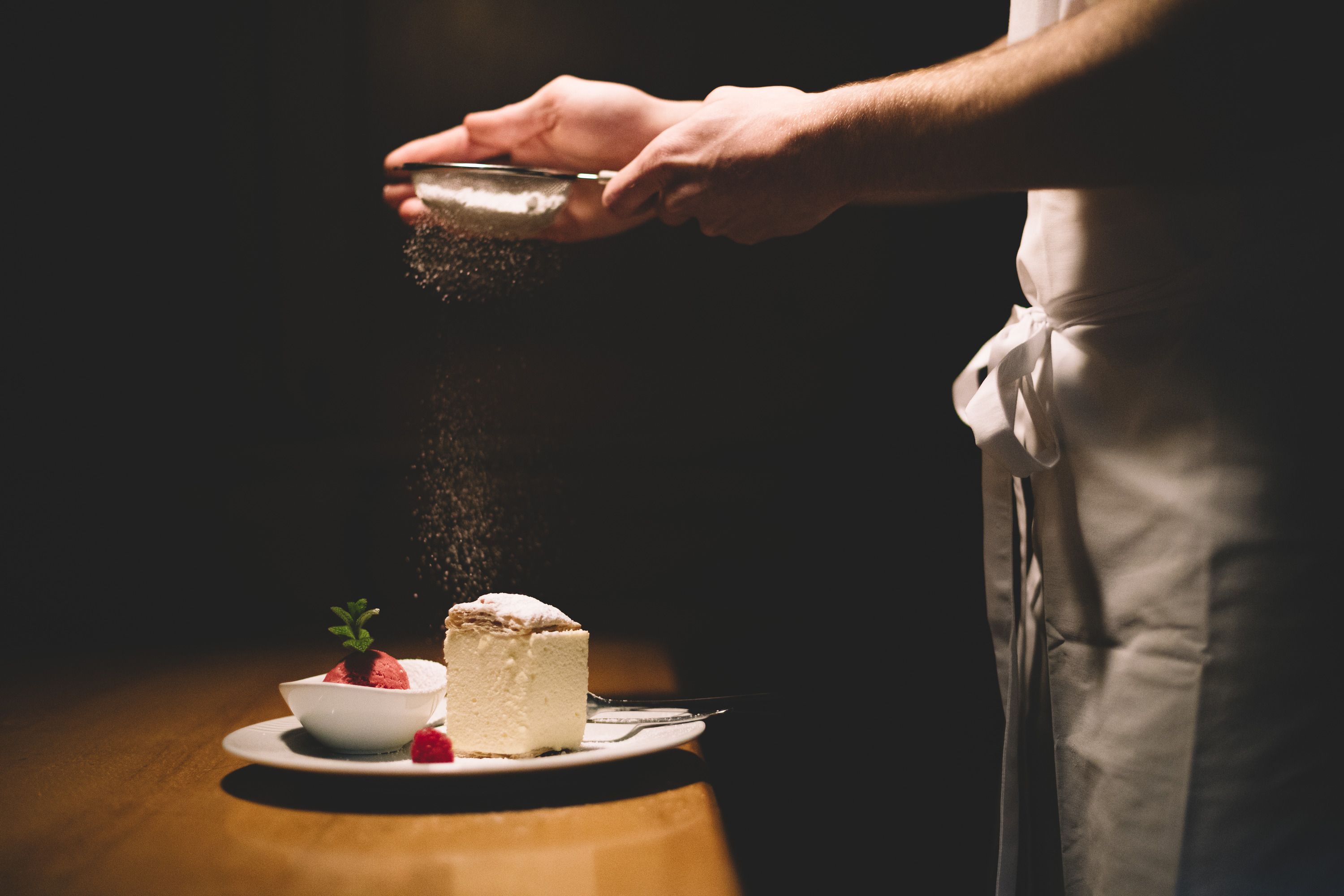 Ein Teller mit Cremeschnitte und Himbeersorbet, darüber wird Puderzucker gestreut.