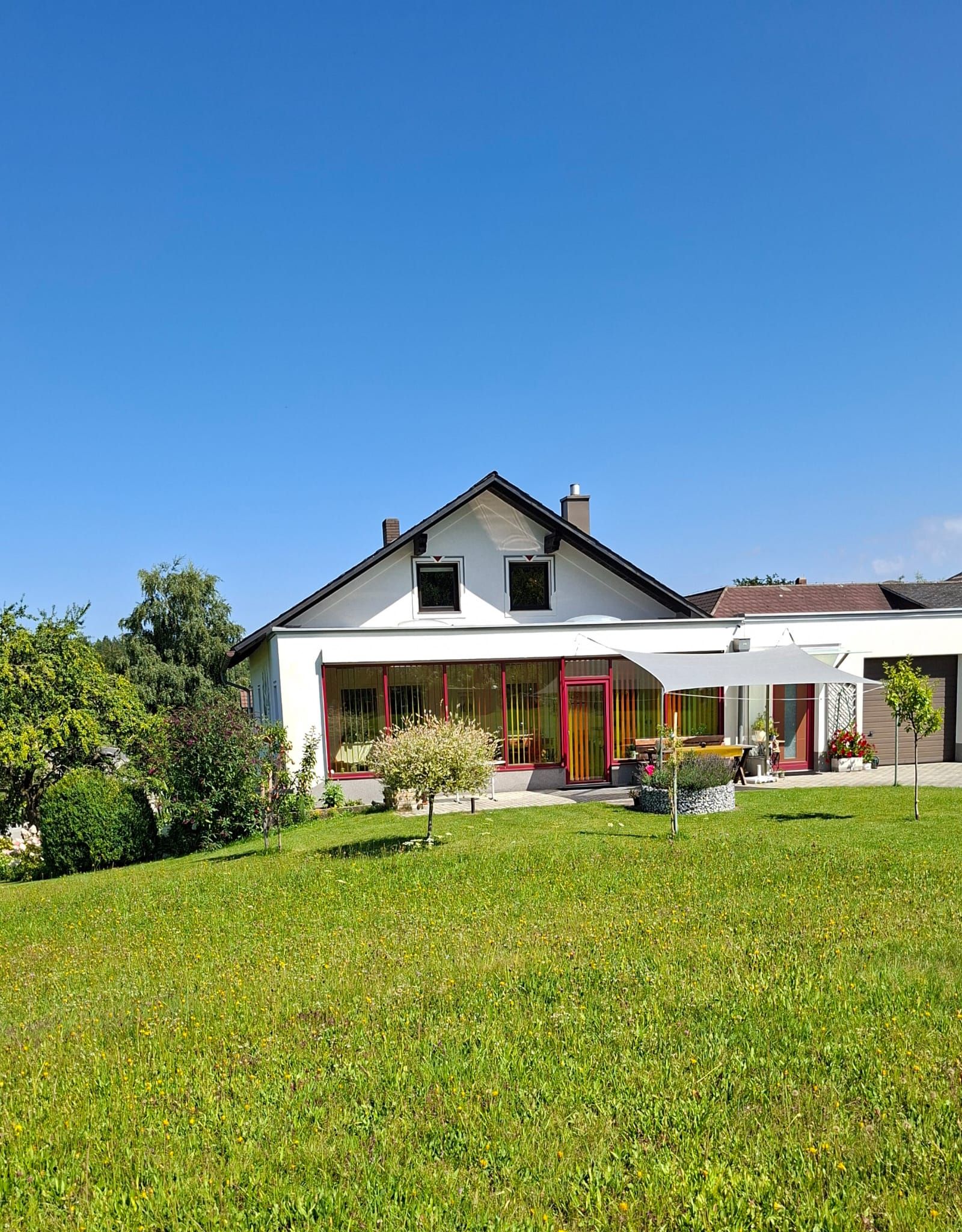 Ein weißes Haus mit rotem Rahmen und Garten vor blauem Himmel.