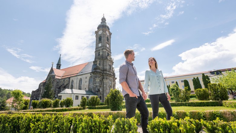 Ein Paar spaziert im Garten des Stifts Zwettl, im Hintergrund die beeindruckende Architektur des Klosters.