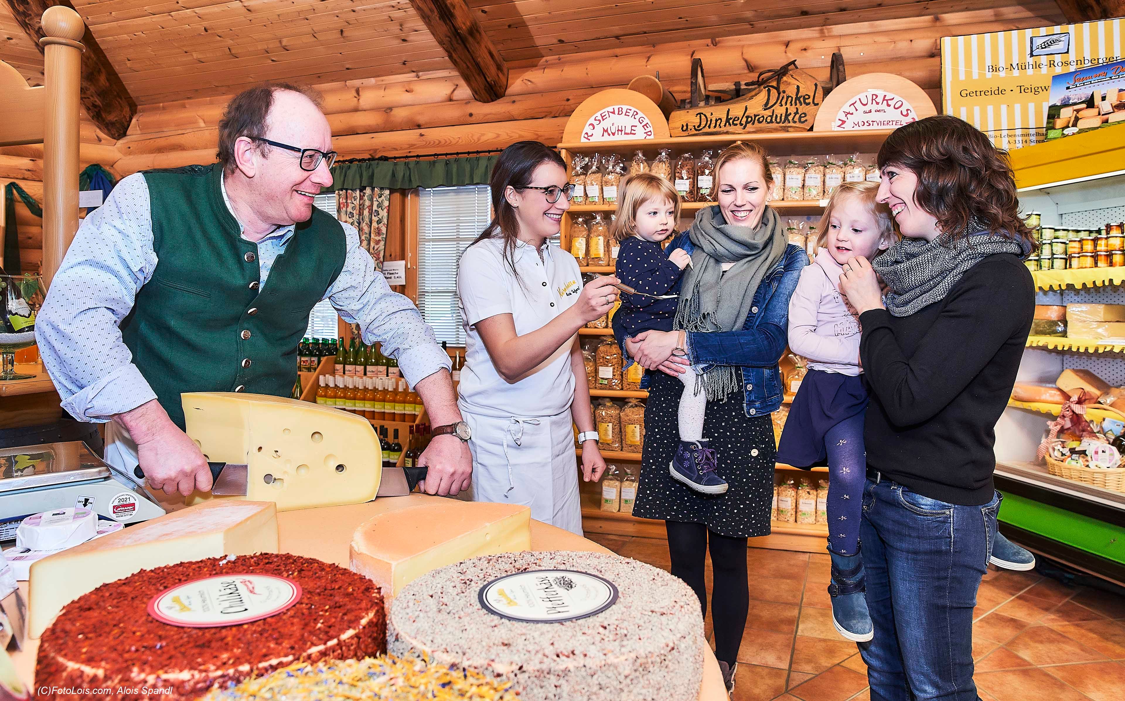 Menschen in einer Käserei, die Käse probieren und lächeln.