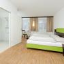 Modernes Hotelzimmer mit Doppelbett, Holzboden und angrenzendem Badezimmer.