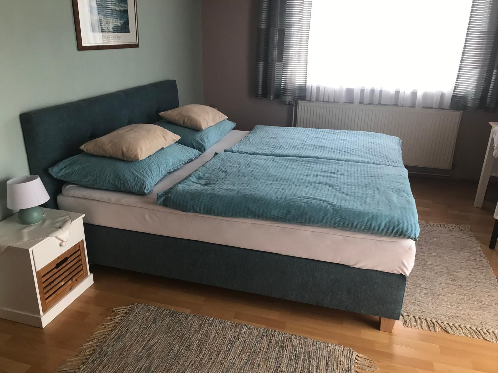 Schlafzimmer mit Doppelbett, blauer Bettwäsche und Nachttisch mit Lampe.