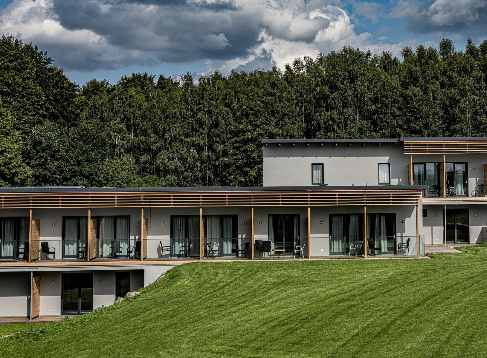 Modernes Hotelgebäude mit Terrasse vor einem Wald.