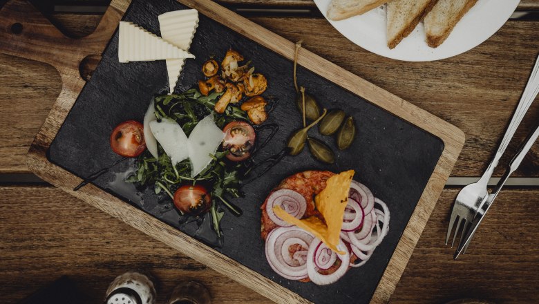 Vorspeisenplatte mit Käse, Salat, Tomaten, Zwiebeln und Kapern auf Holzbrett.
