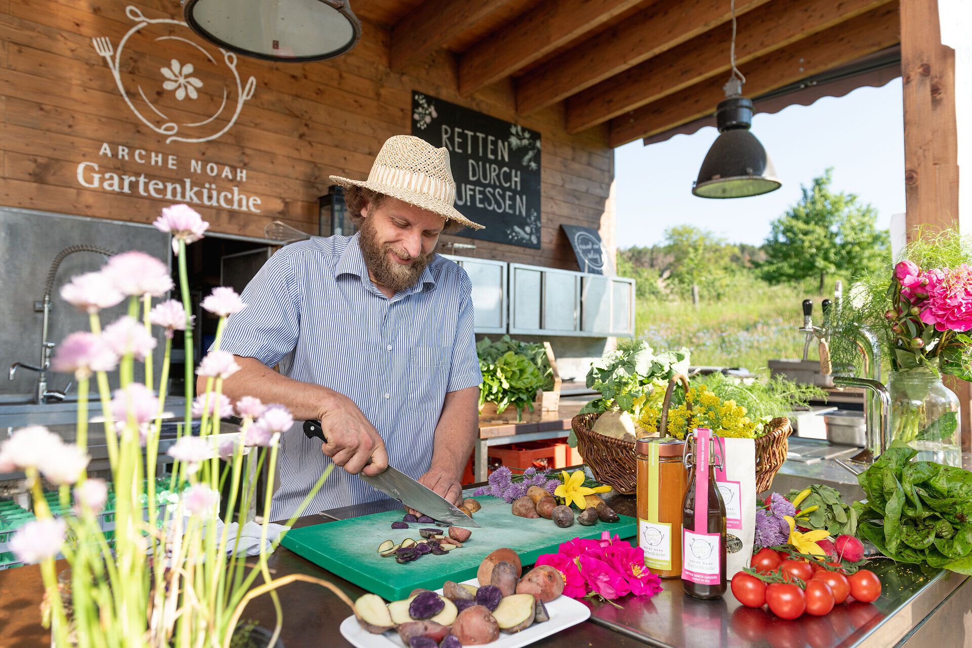 Inmitten eines blühenden Gartens wird frisches Gemüse mit Hingabe zubereitet. Die Farben der Pflanzen und die fröhliche Atmosphäre laden dazu ein, die Köstlichkeiten der Natur zu genießen und die Seele baumeln zu lassen.