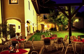 Beleuchteter Außenbereich eines Gasthofs mit gelben Wänden, Tischen und Stühlen auf einer Terrasse bei Nacht.