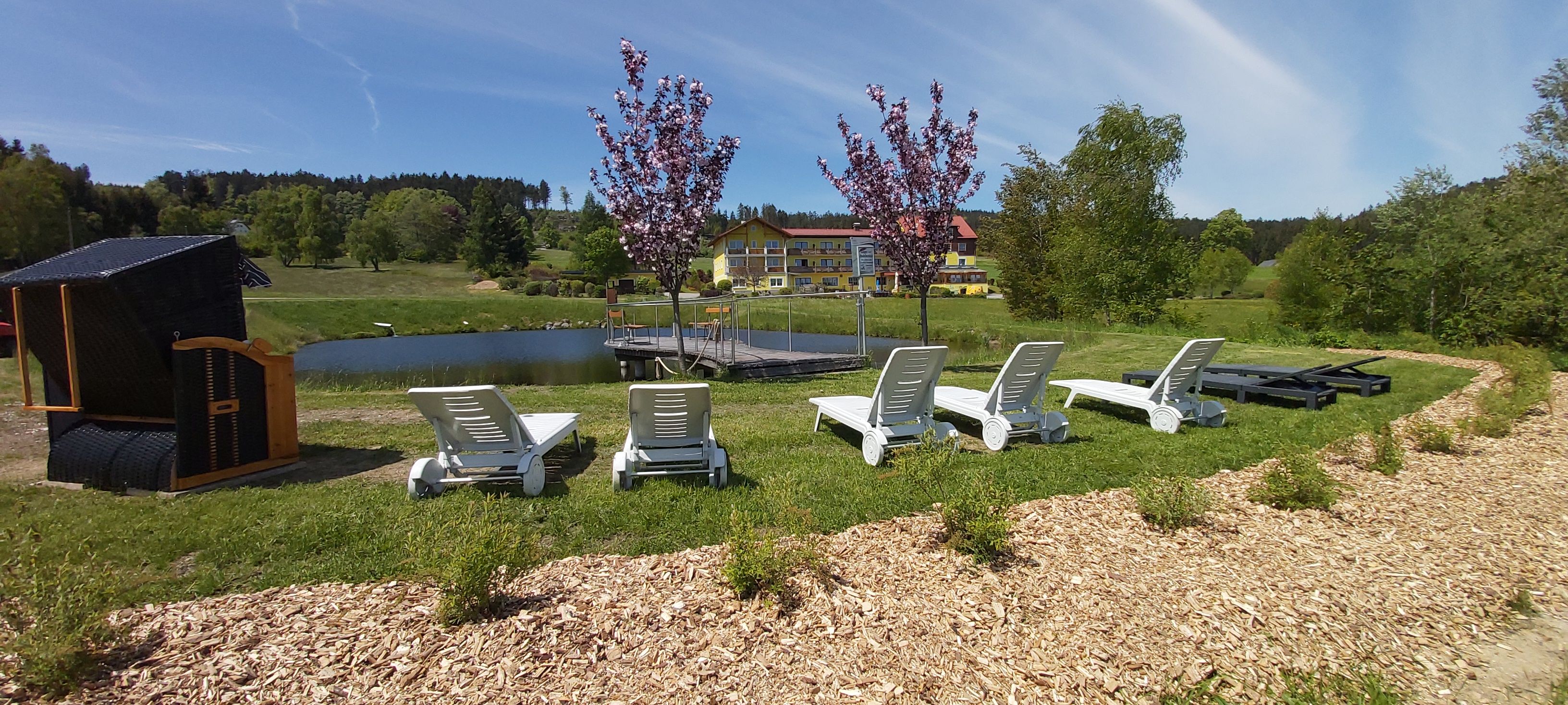 Sonnenliegen am Teich mit Gasthof im Hintergrund.