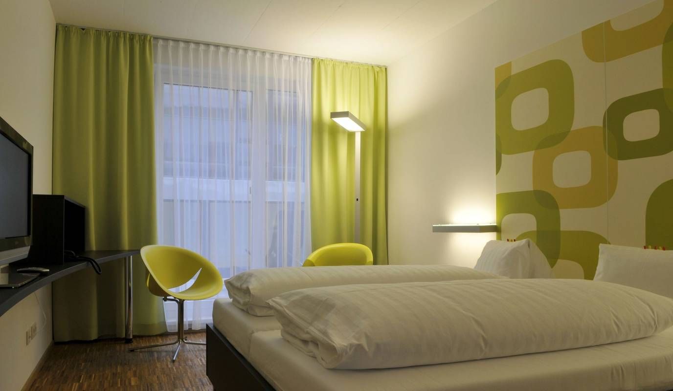 Modernes Hotelzimmer mit Doppelbett, grün-gelben Vorhängen und Wanddekor.
