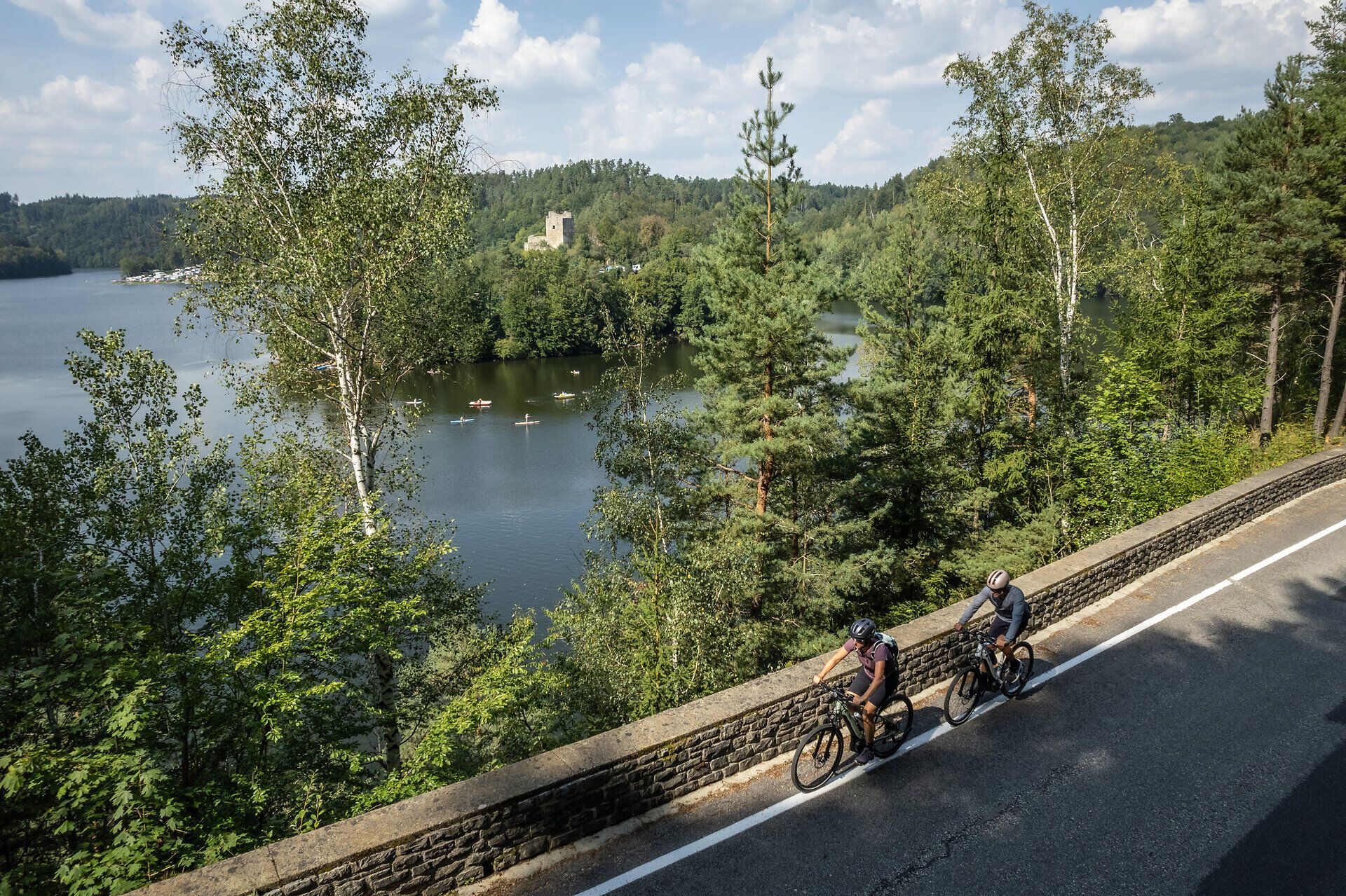 Radfahrer gleiten entlang des malerischen Kamptal Radwegs, umgeben von üppigem Grün und glitzerndem Wasser. Die sanften Hügel im Hintergrund und die historische Ruine Dobra verleihen der Szenerie einen Hauch von Romantik und Abenteuer. Hier wird der Sommer in den Bergen zum unvergesslichen Erlebnis.