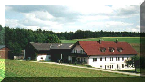 Ein traditioneller Bauernhof mit roten Dächern in einer ländlichen Umgebung, umgeben von grünen Feldern und Wäldern.