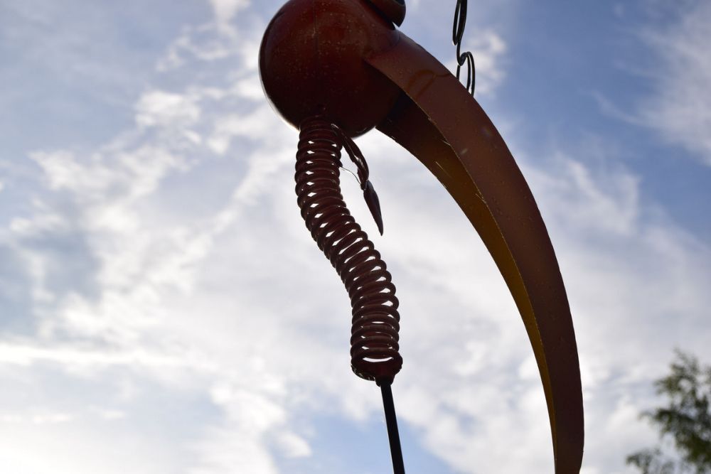 Nahaufnahme einer Metallskulptur mit spiralförmigem Element vor bewölktem Himmel.