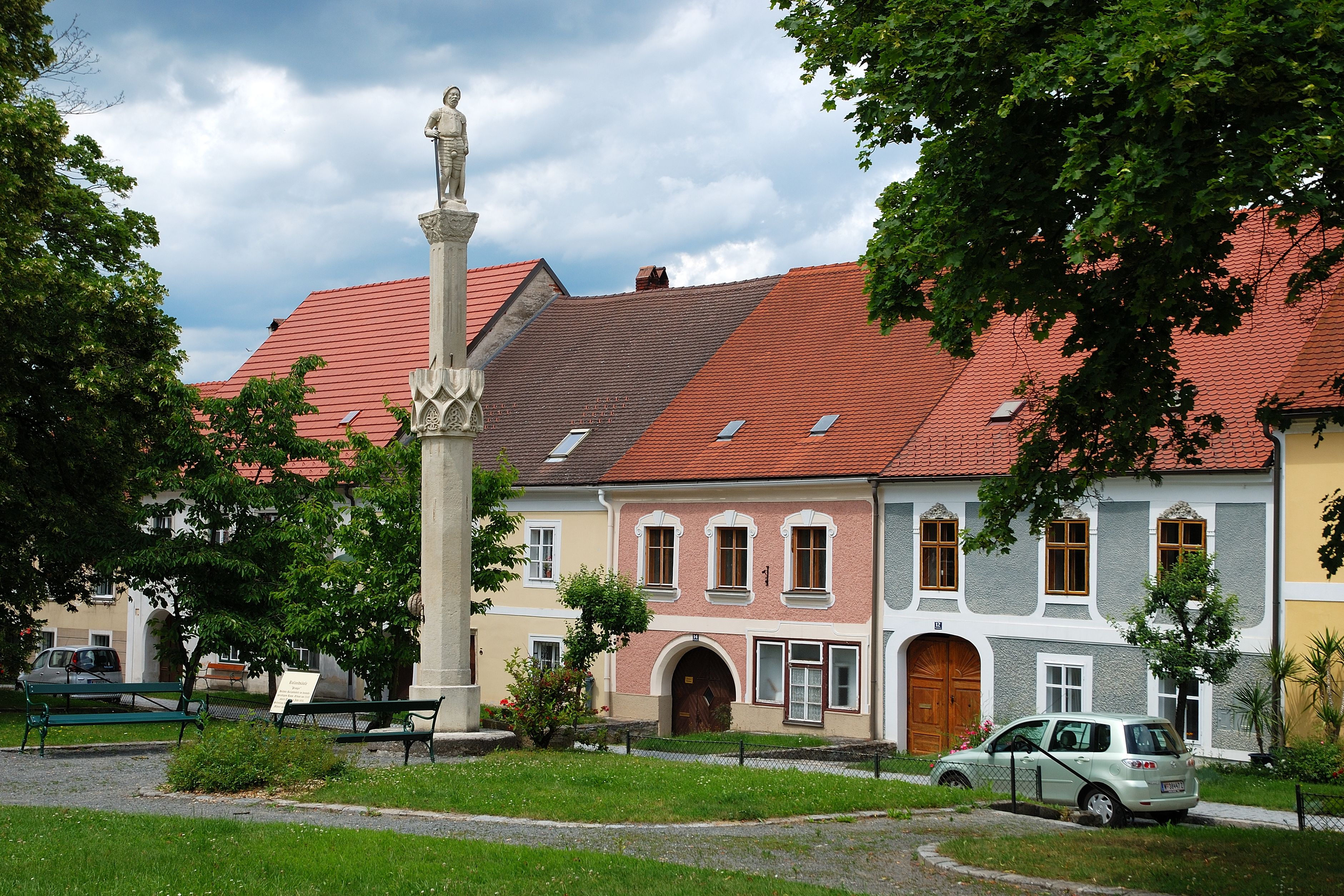 Statue auf einer Säule vor bunten Häusern in Drosendorf-Zissersdorf.