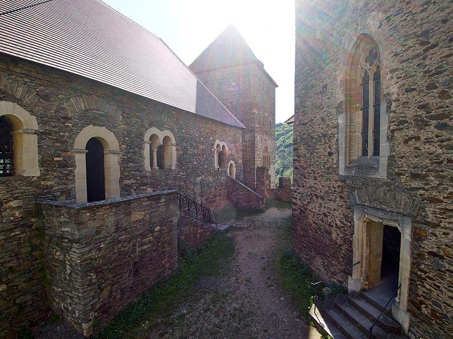 Innenhof der Burg Hardegg mit alten Steinmauern und gotischen Fenstern, Sonnenstrahlen im Hintergrund.