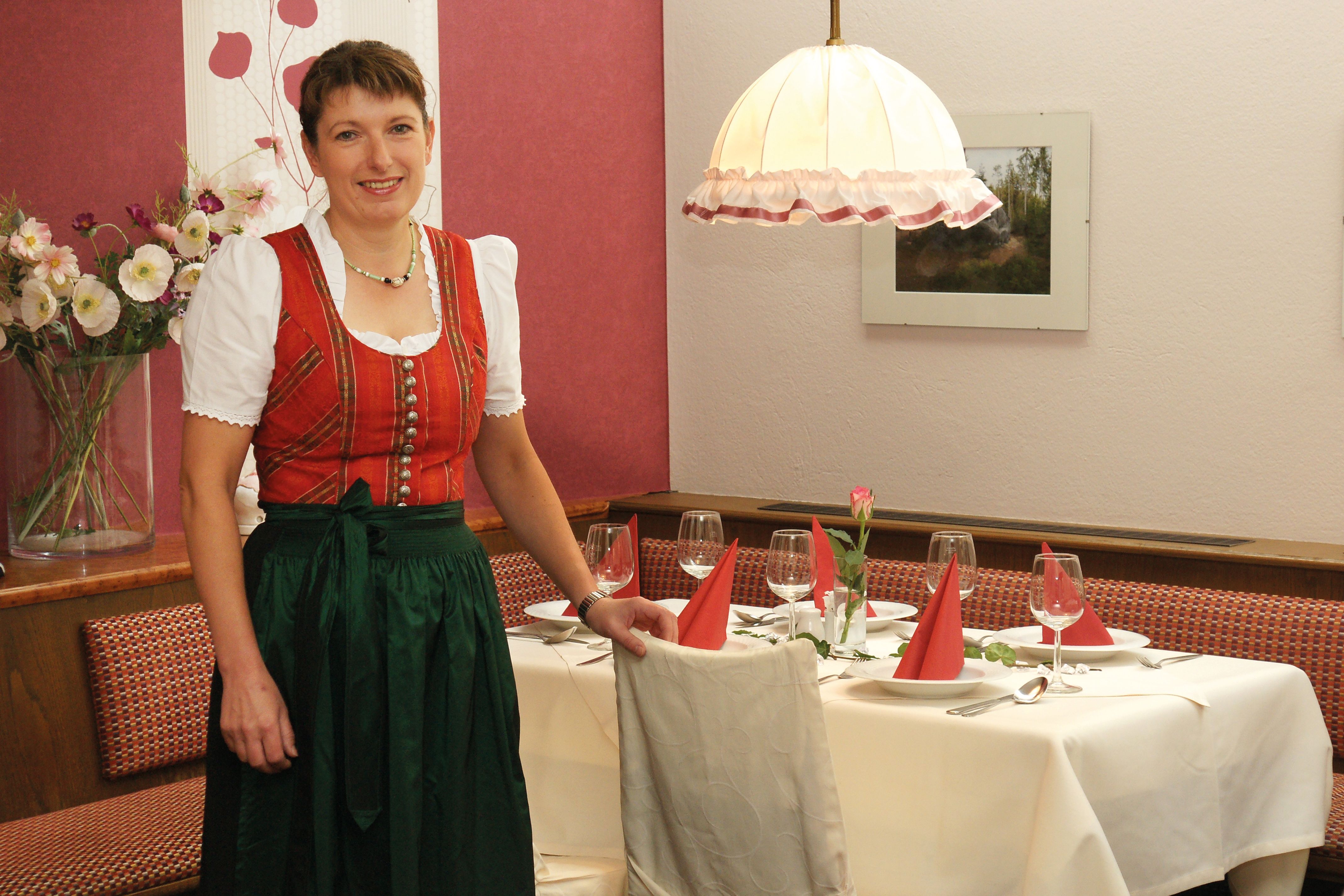 Eine Frau in traditioneller Kleidung steht neben einem gedeckten Tisch in einem Restaurant.