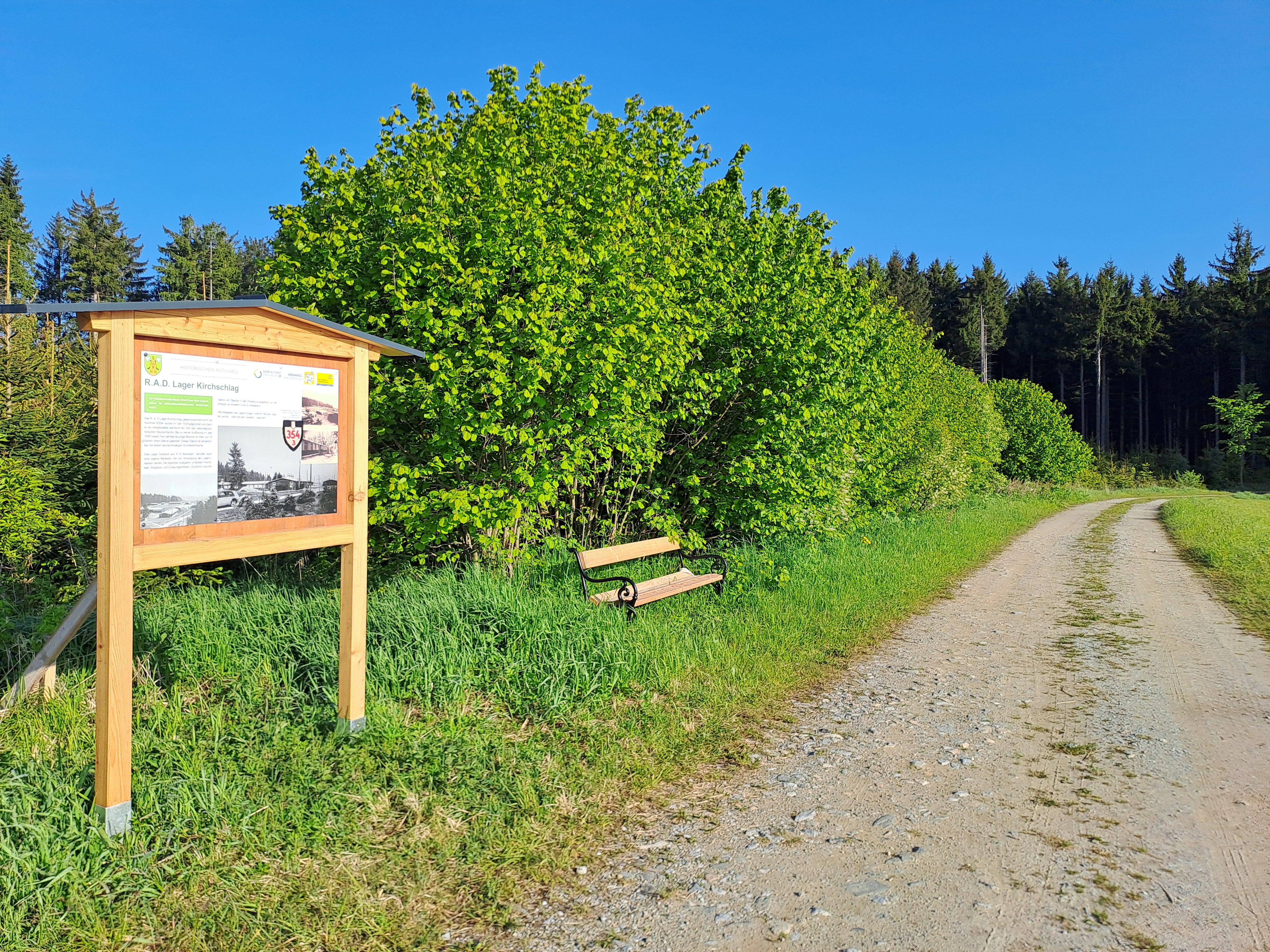 Eine Infotafel entlang eines Feldwegs neben Wiesen.