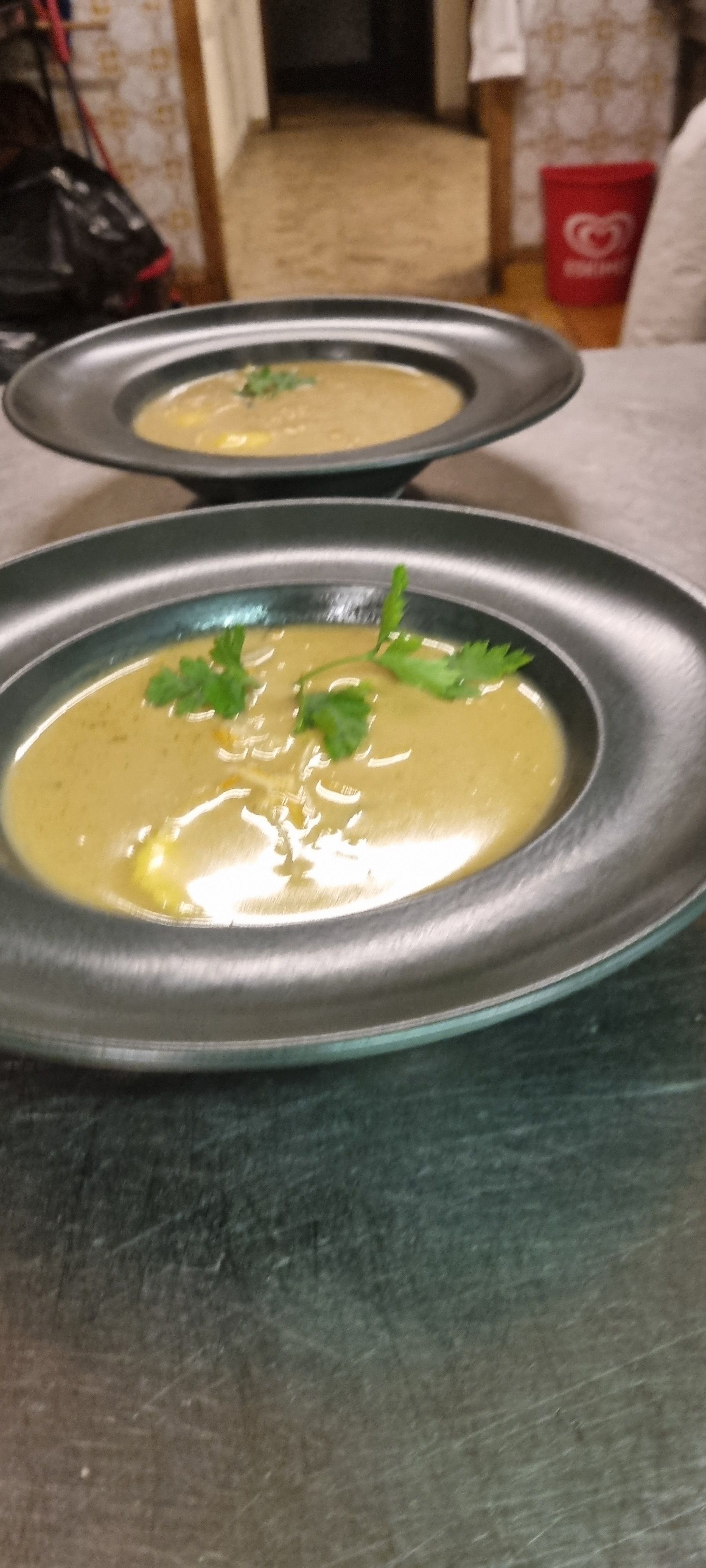 Zwei schwarze Teller mit Suppe und Petersiliengarnitur auf einem Tisch.