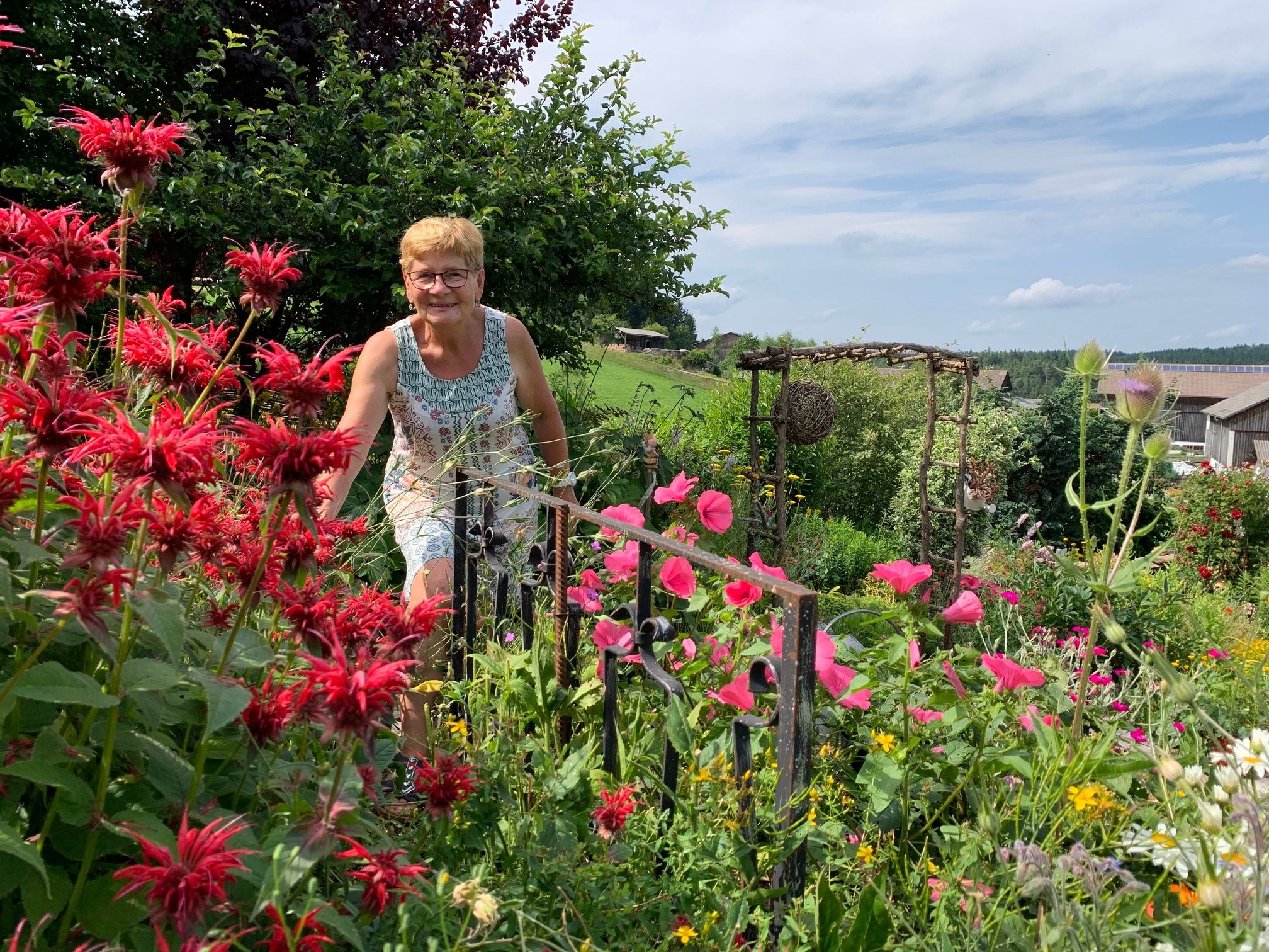 Frau in einem blühenden Garten mit roten und rosa Blumen.