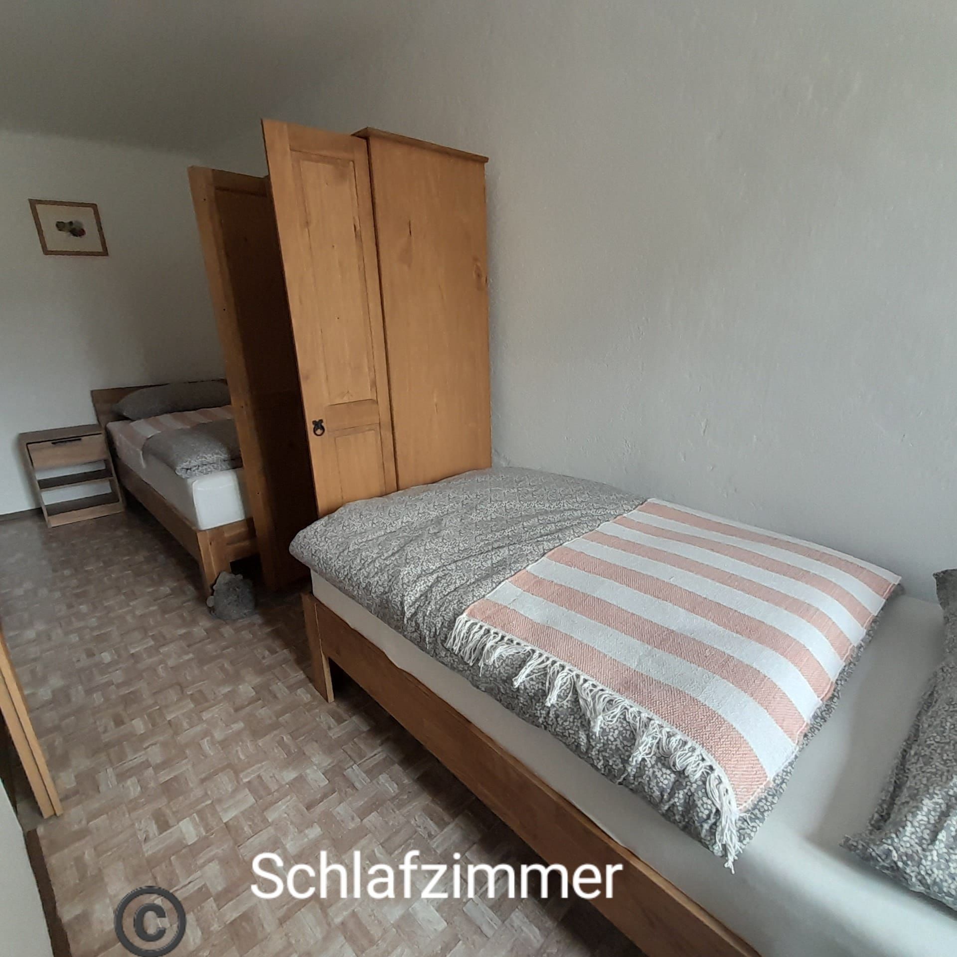 Schlafzimmer mit zwei Einzelbetten, Holzmöbeln und einem Nachttisch.