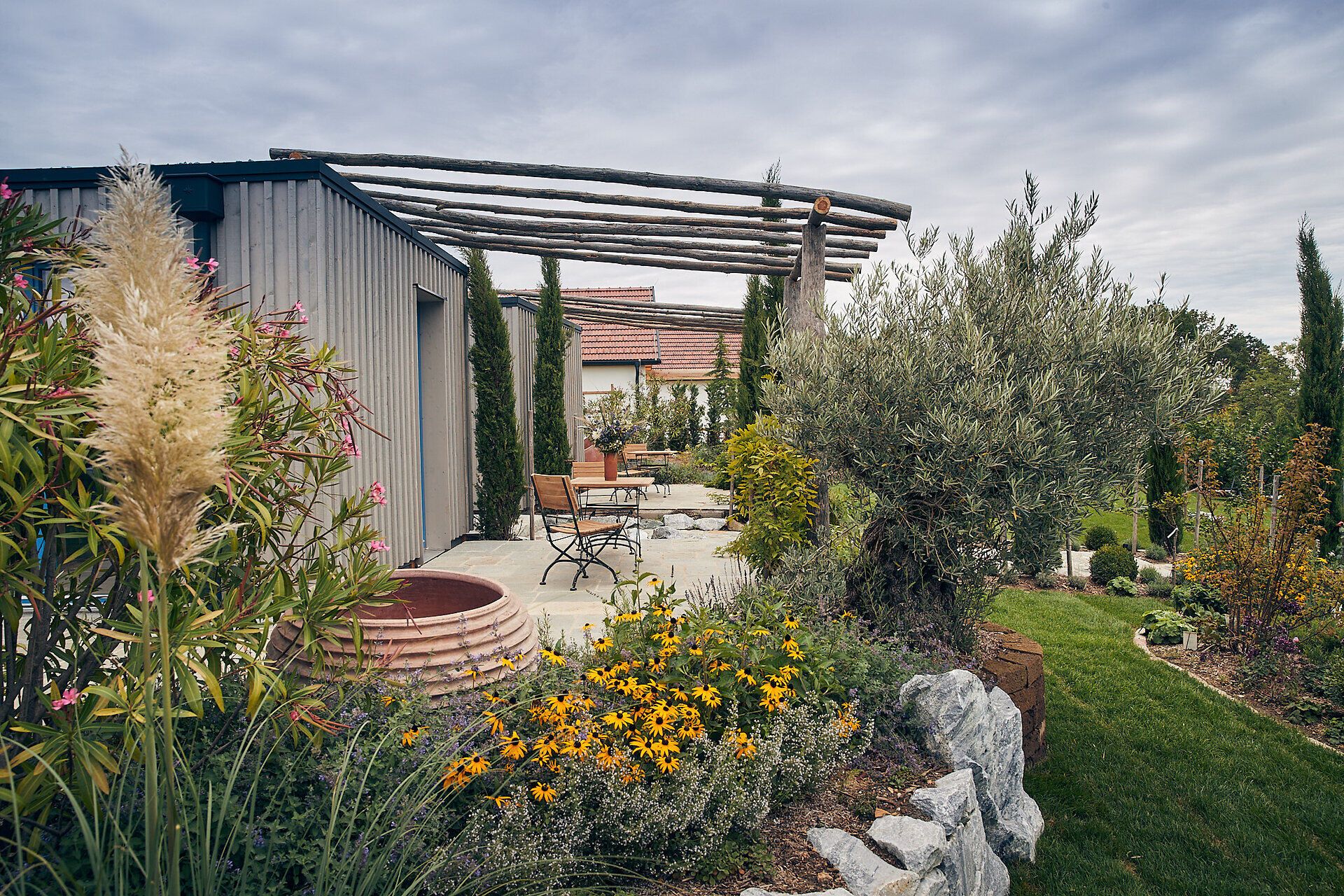 Umgeben von üppigen Blumenbeeten und sanften Hügeln strahlt die Villa eine einladende Ruhe aus. Die harmonische Verbindung von Natur und Architektur lädt dazu ein, die Seele baumeln zu lassen und die Schönheit des Gartens zu genießen.