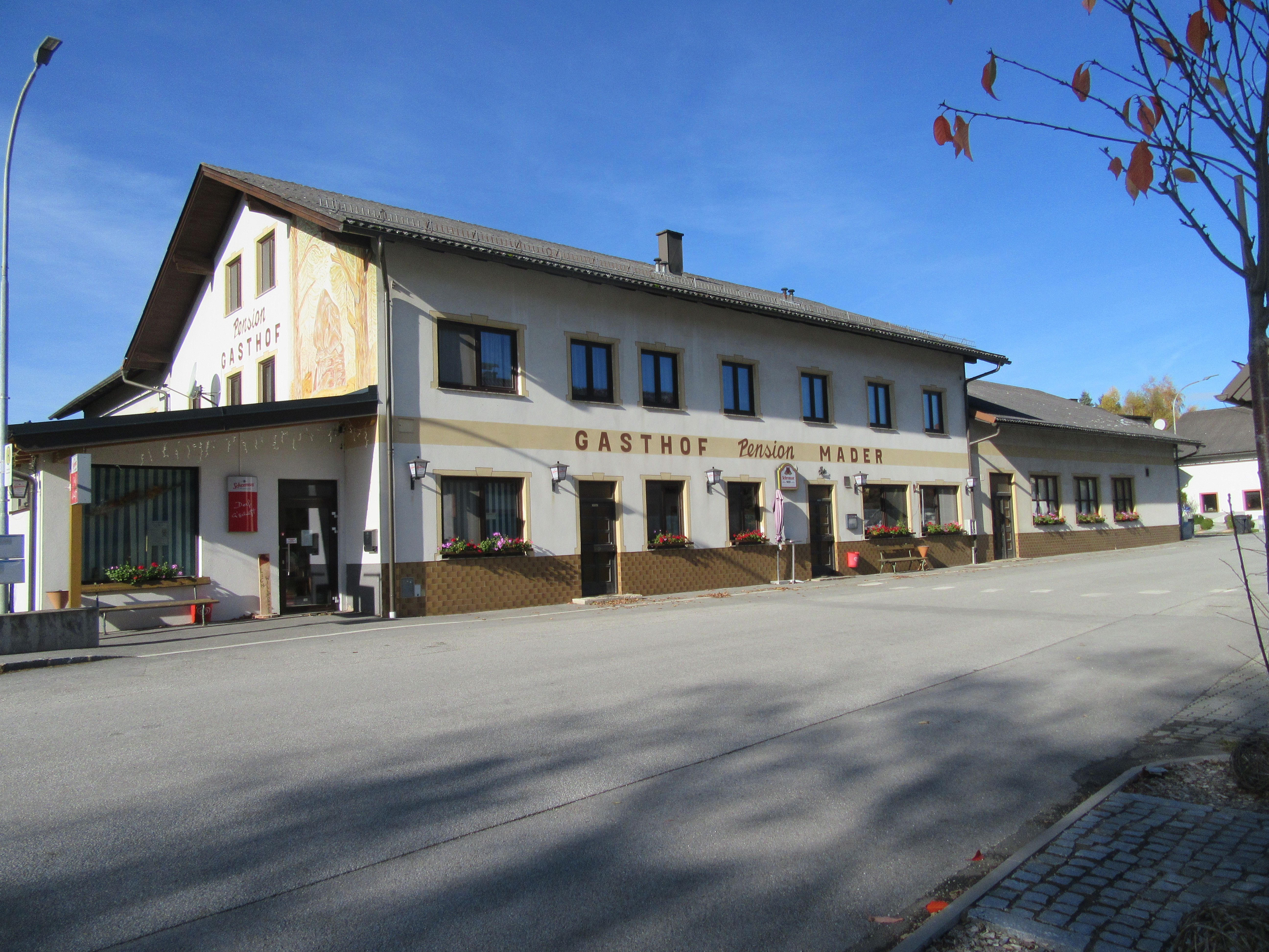 Gasthof Mader an einer ruhigen Straße mit blühenden Blumenkästen und blauem Himmel.
