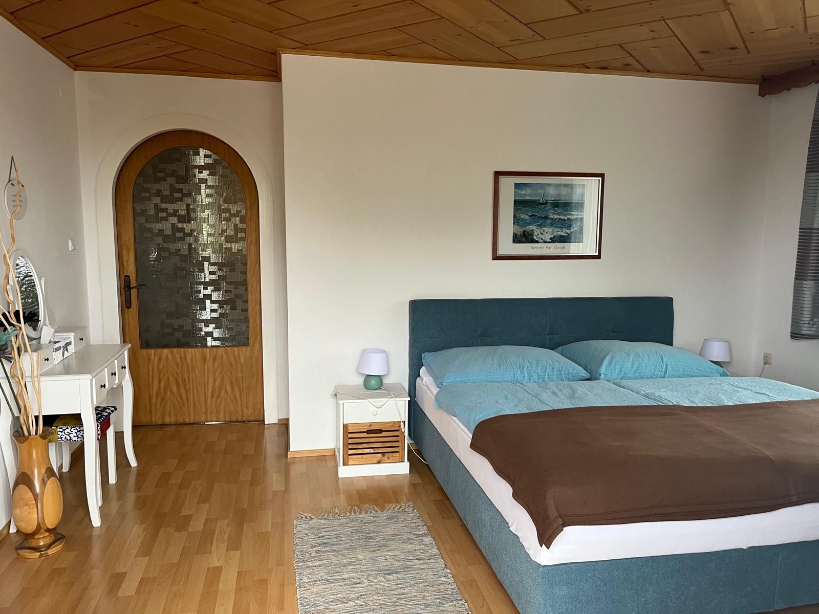 Schlafzimmer mit Doppelbett, Kommode und Holztür.